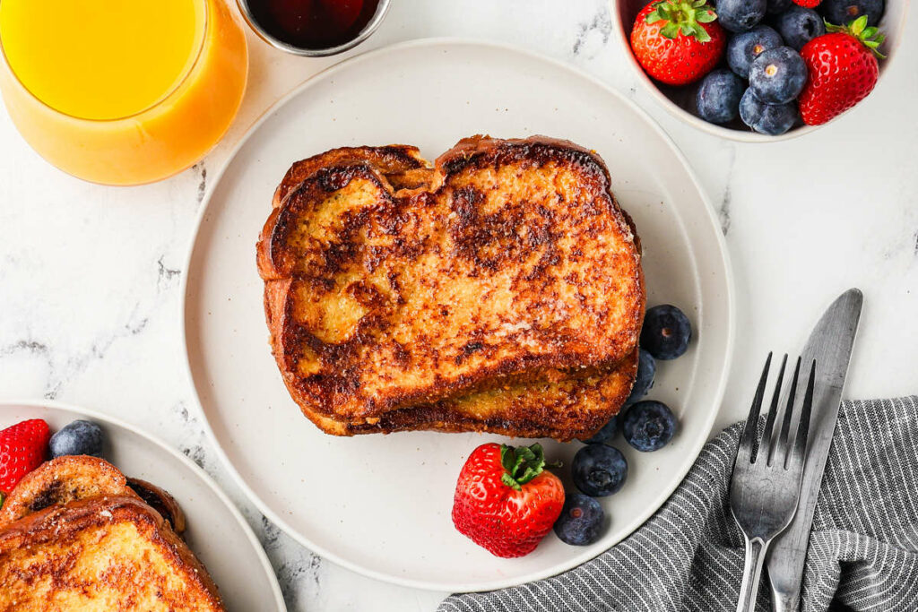 A plate with homemade french toast and berries next to a glass of orange juice.