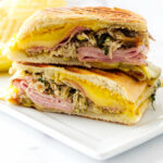 A pressed Cuban sandwich on a plate with potato chips.