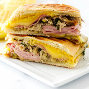 A pressed Cuban sandwich on a plate with potato chips.