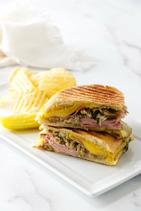 A homemade cuban sandwich on a dinner plate with chips.