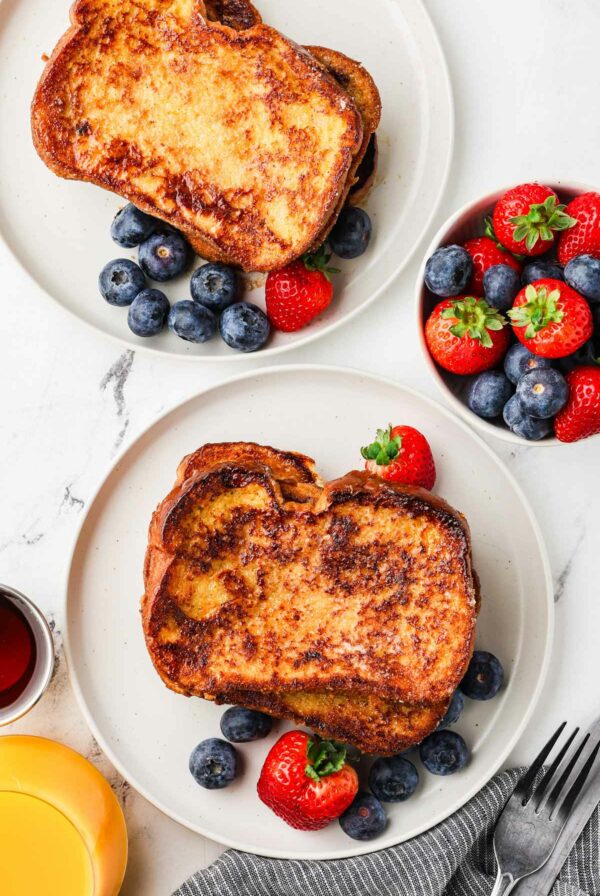 Two breakfast plates stacked with slices of traditional french toast and berries.