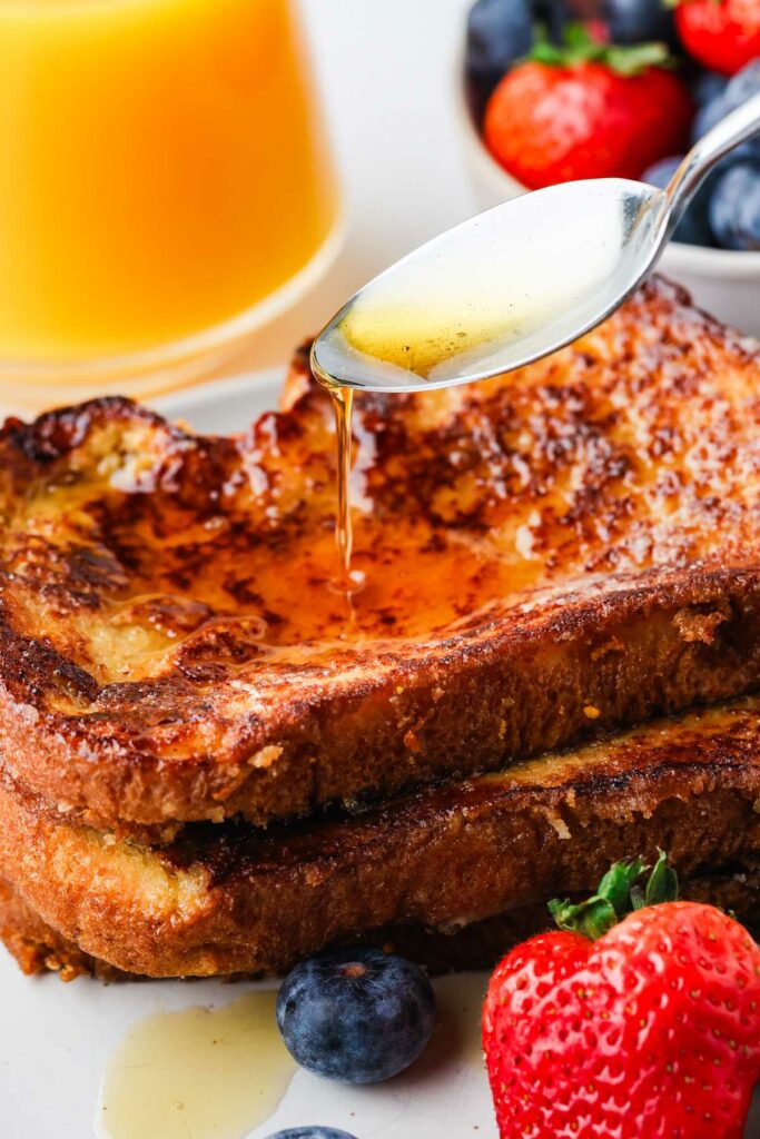 Drizzling maple syrup over the top of two slices of classic french toast.