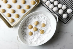 Rolling warm Christmas cookies in confectioners sugar.