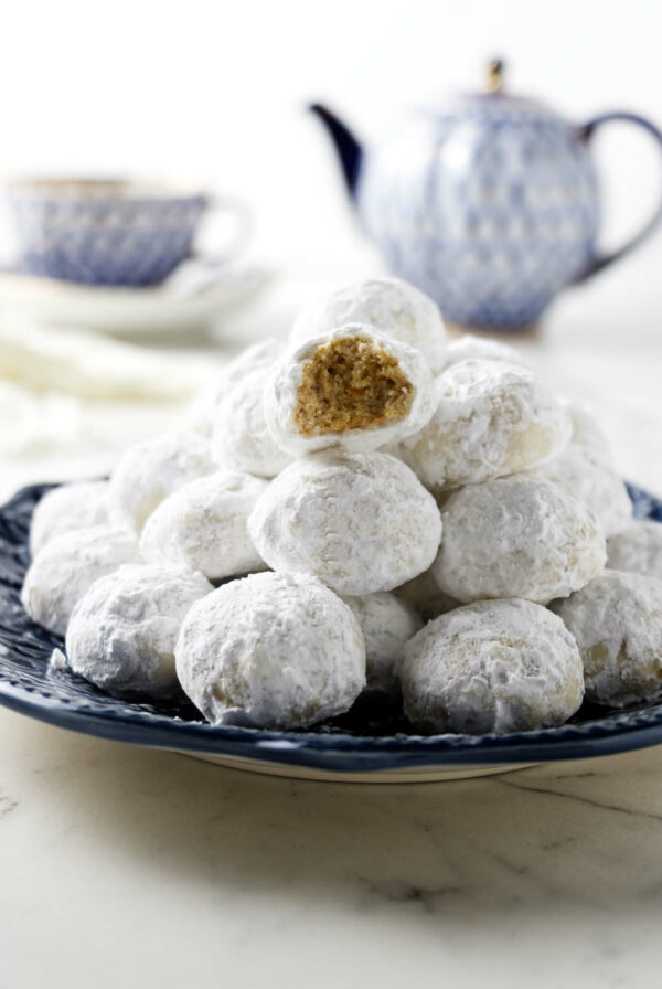 A plate filled with Christmas wedding cookies in front of a tea pot.