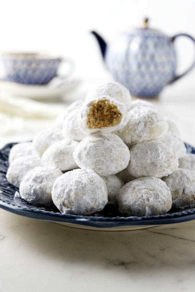A plate filled with Christmas wedding cookies in front of a tea pot.