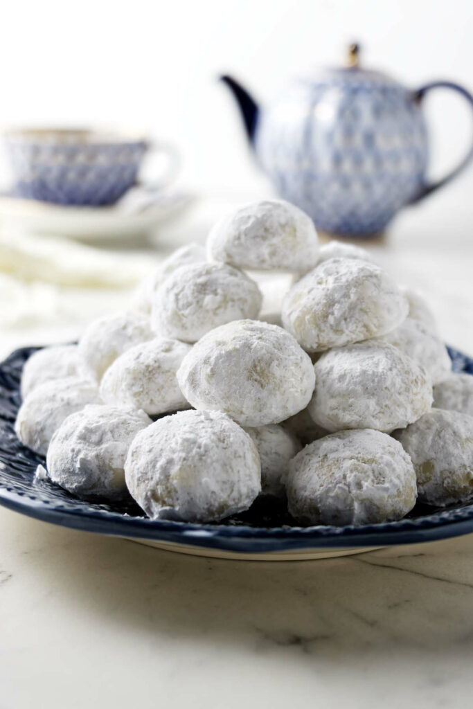 Italian cookie with powdered sugar on a plate in front of a cup of tea and a tea pot.