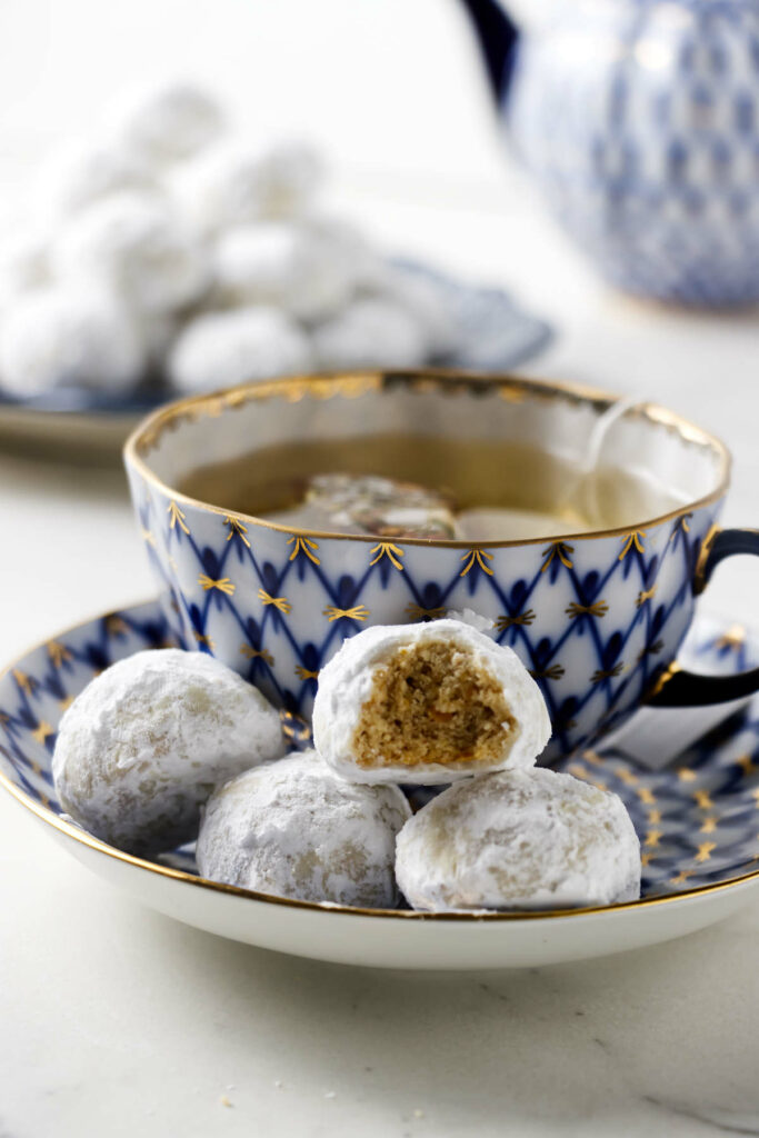 Several wedding almond cookies on a dish in front of a cup of tea.