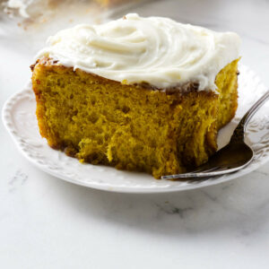 A pumpkin cinnamon roll on a dessert plate topped with cream cheese icing.