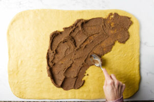Spreading a cinnamon butter mixture on homemade pumpkin roll dough.