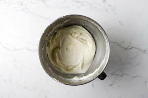 Mixing cream cheese frosting in a metal mixing bowl.