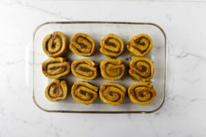 Slices of pumpkin roll dough in a baking dish.
