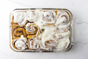 Spreading cream cheese glaze over pumpkin rolls.