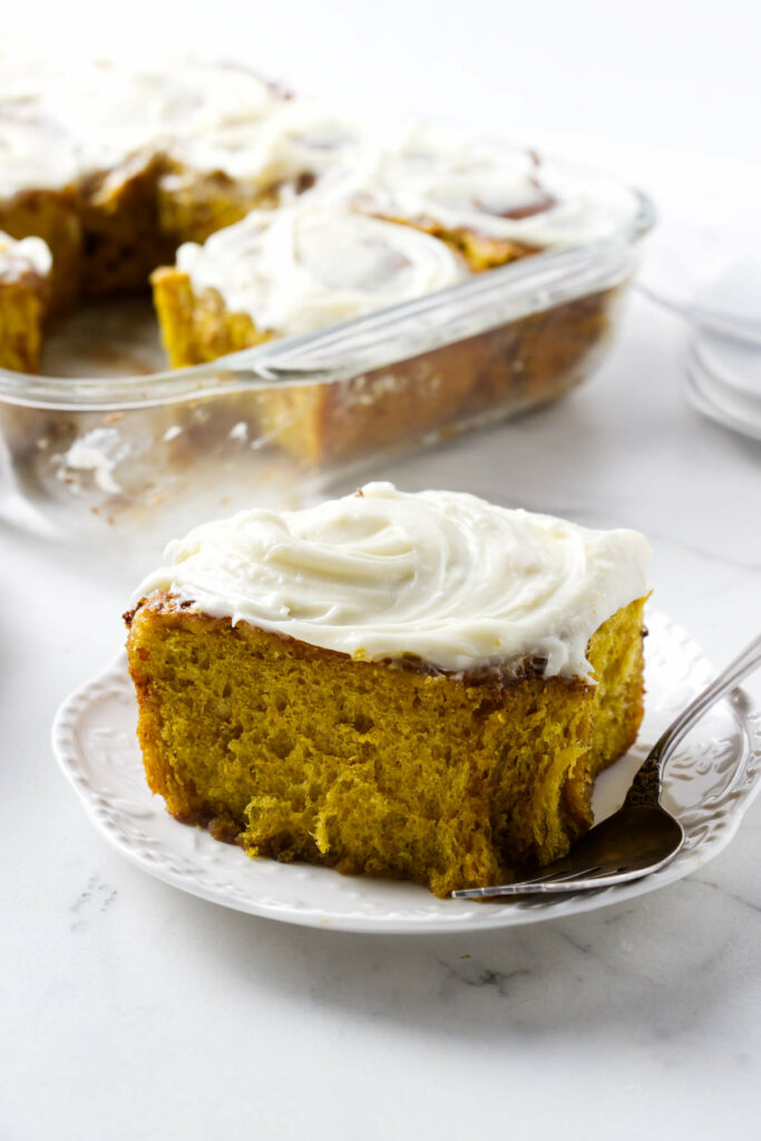 A plate with a pumpkin cinnamon bun in front of a dish with more rolls.
