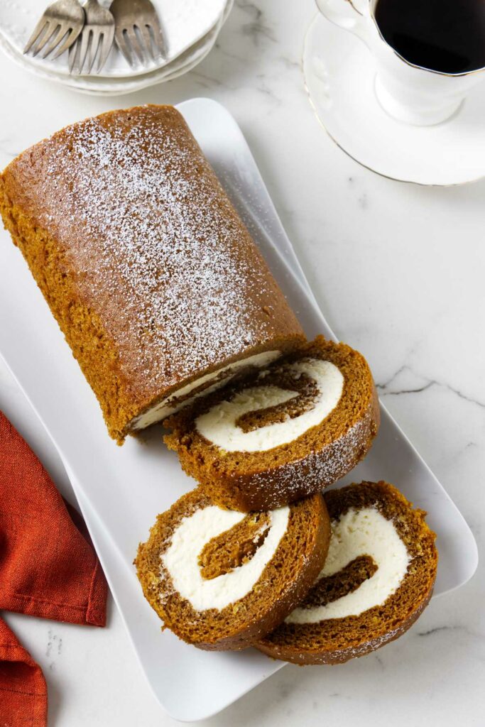 A pumpkin roll on a plate with three slices next to a cup of coffee.