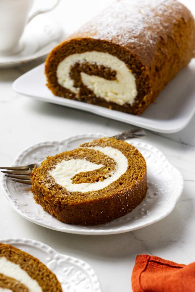 A pumpkin swiss roll cake with a slice in front.