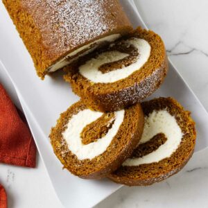 A partially sliced pumpkin roll filled with cream cheese frosting.