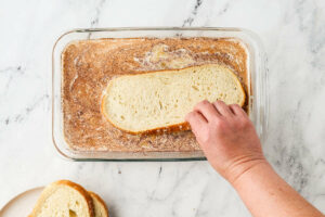 Dipping a slice of sourdough bread in an egg custard mixture.