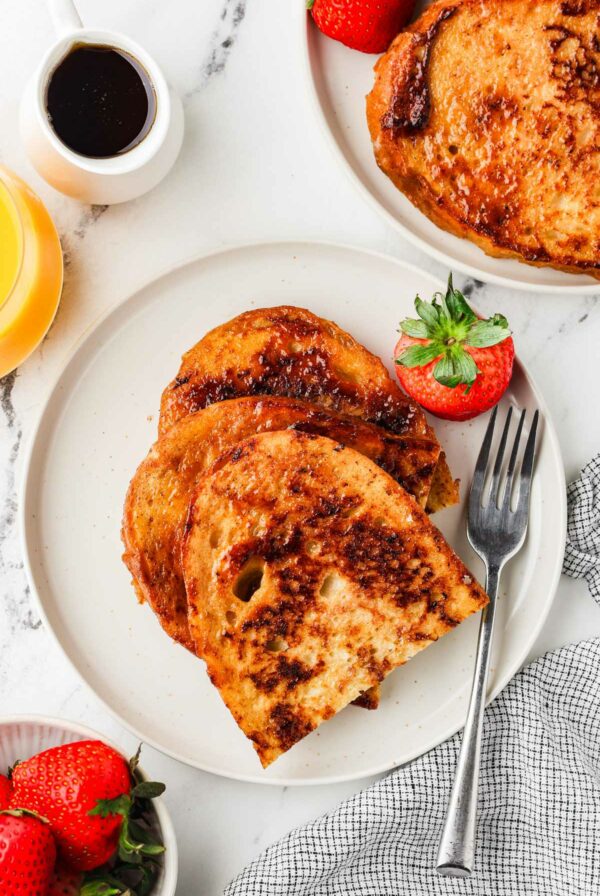 Two breakfast plates filled with sourdough french toast next to fresh strawberries.