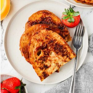 A plate filled with french toast with sourdough bread and a strawberry.
