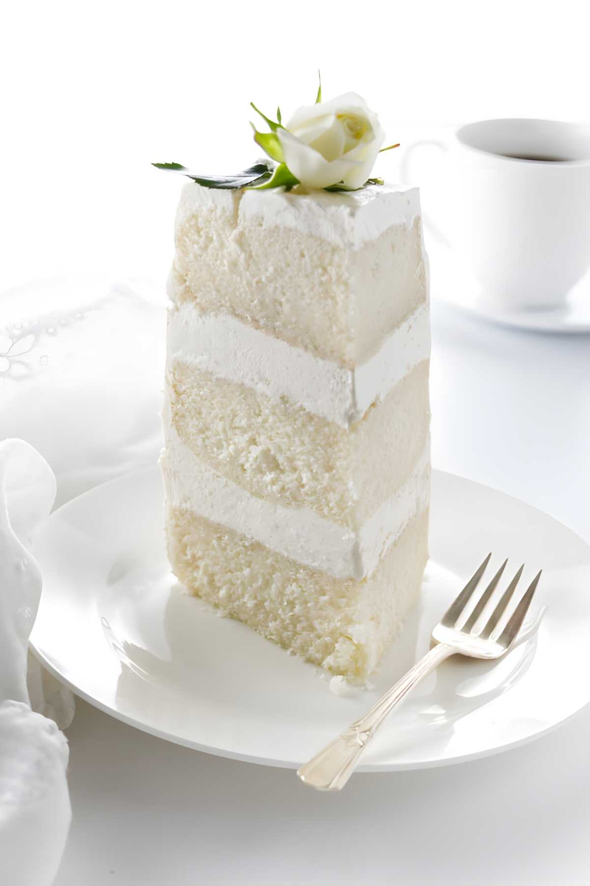 Slice of white layer cake with rose on plate, fork beside it.
