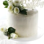 White cake with white roses and Happy Birthday sign on cake stand.