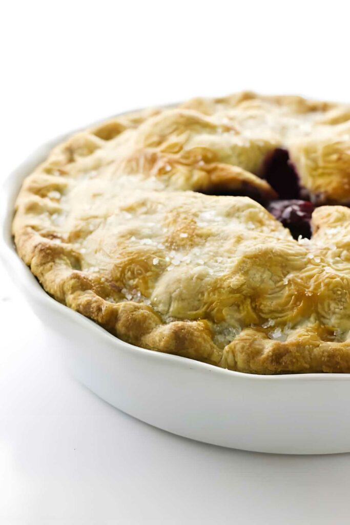 Homemade golden-brown fruit pie with flaky crust in a white ceramic dish.