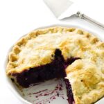 Blueberry rhubarb pie with a golden crust in a dish, slice missing, server nearby.