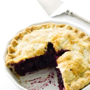 Blueberry pie with a golden crust in a dish, slice missing, server nearby.