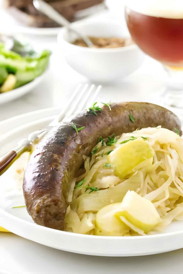 Cooked bratwurst on sauerkraut and apples, garnished with herbs on a plate.