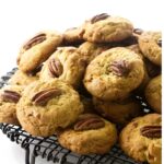 Fresh pecan-topped cookies on a black cooling rack against a white background.