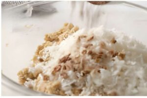 Close-up of ingredients being mixed in a glass bowl, some poured from above.