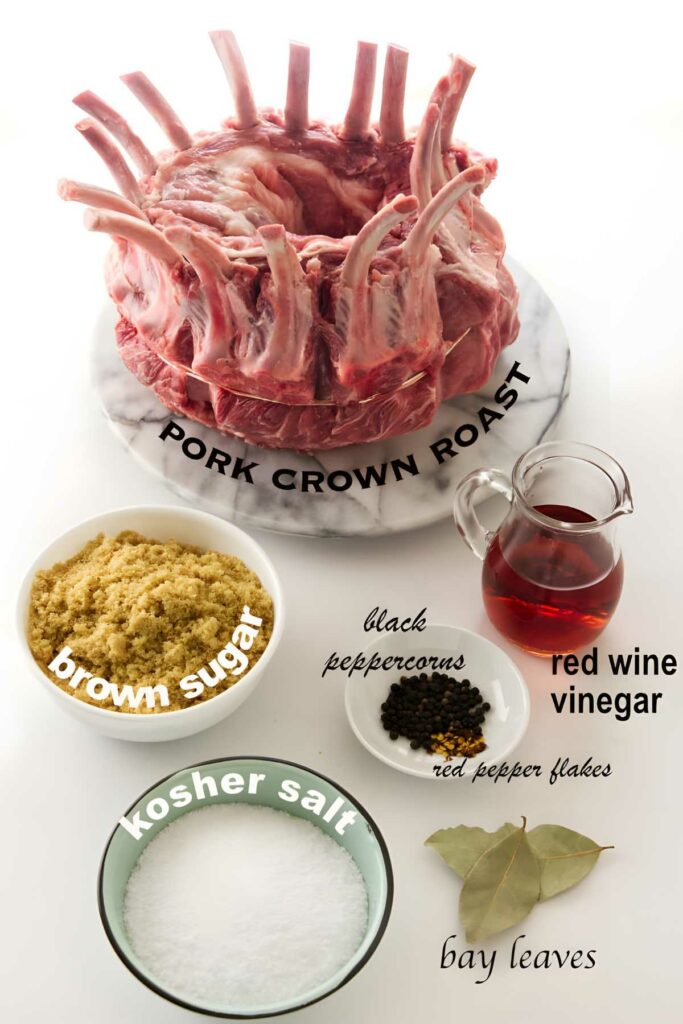 Raw pork crown roast on marble platter with assorted seasonings and red wine vinegar.