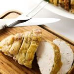 Sliced roasted turkey breast on a wooden cutting board with utensils.