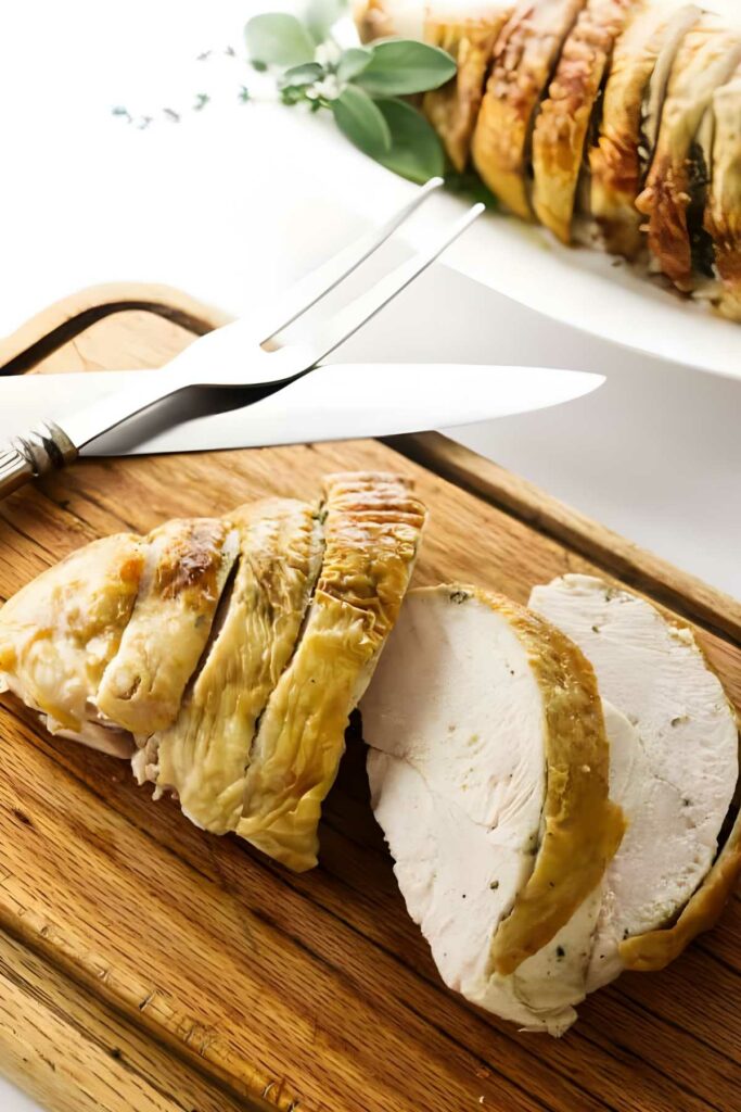 Sliced roasted turkey breast on a wooden cutting board with utensils.
