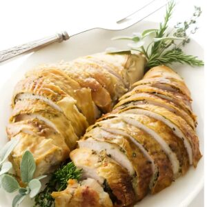 Sliced roasted turkey breast on white platter with fresh herb garnish.