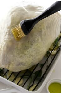 Raw turkey breast on rack, brushed with oil; herbs and lemons beneath.