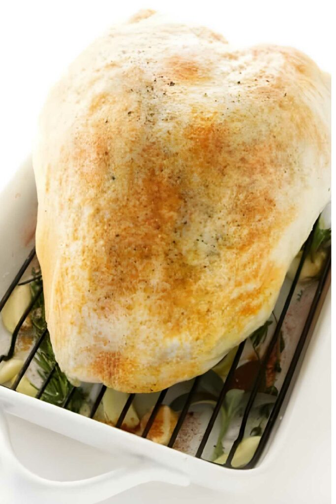 Golden baked turkey breast on a roasting rack, garnished with fresh herbs.