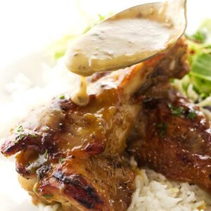 Spoon pours gravy over roasted turkey wing on rice, greens behind.