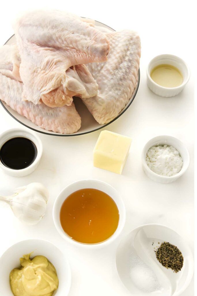 Raw turkey wings in a bowl, surrounded by assorted small condiment bowls.