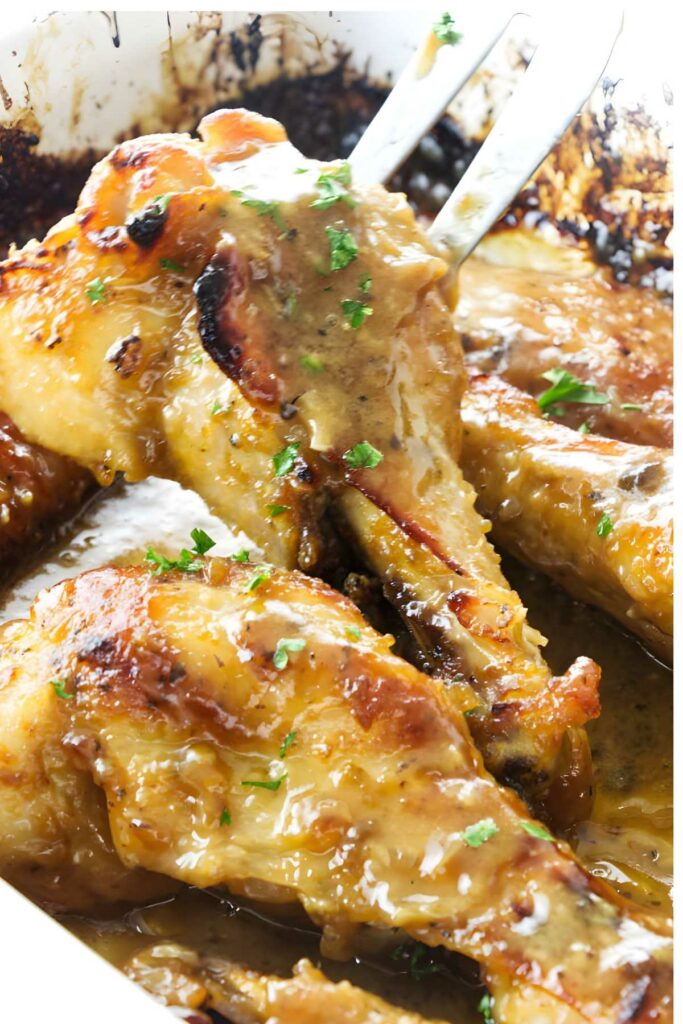 Tongs lift golden, saucy turkey wings with parsley from a baking dish.