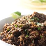 Shredded beef topped with cilantro in a white bowl, lime on side.