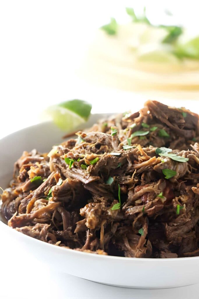 Shredded beef topped with cilantro in a white bowl, lime on side.