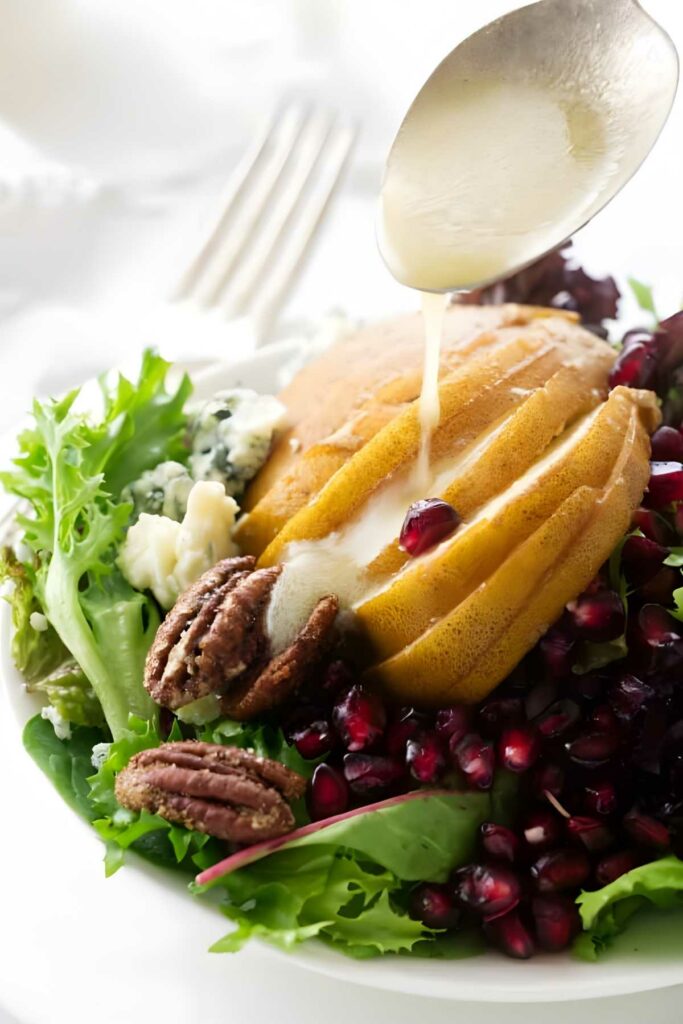 Salad with pear, pomegranate, cheese, pecans, greens; dressing poured on top.