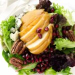 Salad with mixed greens, pear, blue cheese, pecans, and pomegranate on plate.