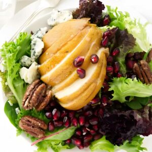 Salad with mixed greens, pear, blue cheese, pecans, and pomegranate on plate.