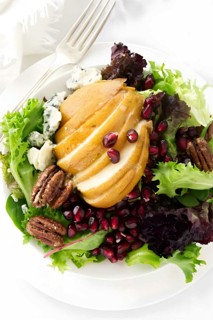 Salad with mixed greens, pear, blue cheese, pecans, and pomegranate on plate.