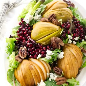 Pear and blue cheese salad with pomegranate, pecans, and greens on white plate.