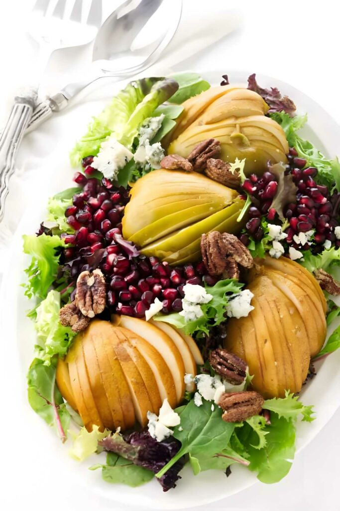 Pear and blue cheese salad with pomegranate, pecans, and greens on white plate.
