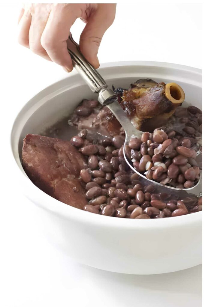 Hand serving beans, meat, and ham bone from broth with slotted spoon.