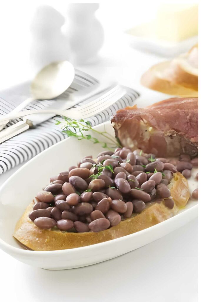 Red beans on bread with ham and herbs on a white dish.